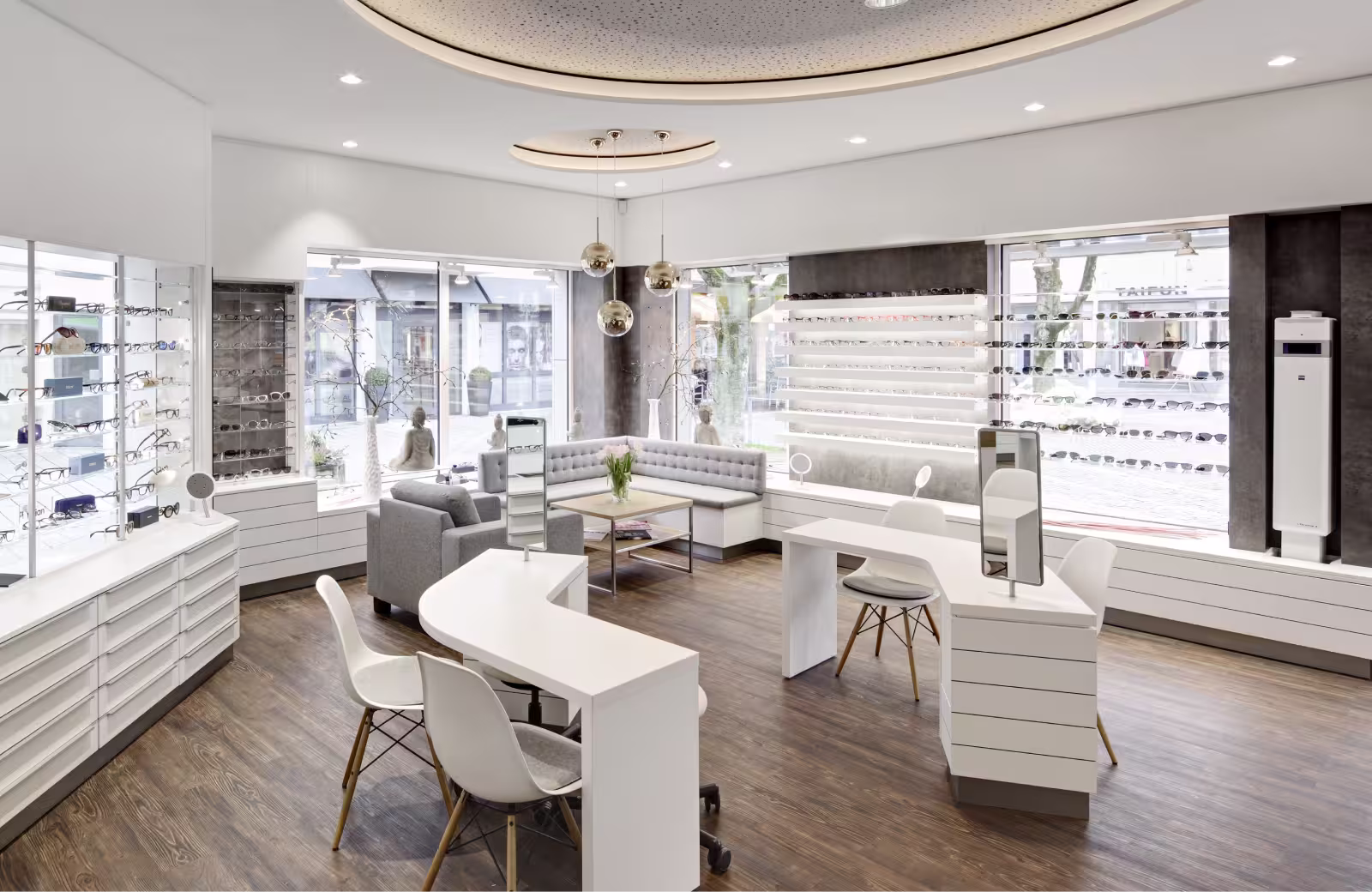 Helles, modernes Optikgeschäft mit weißen Möbeln, Holzboden und Wanddisplays mit Brillen und Sonnenbrillen.
