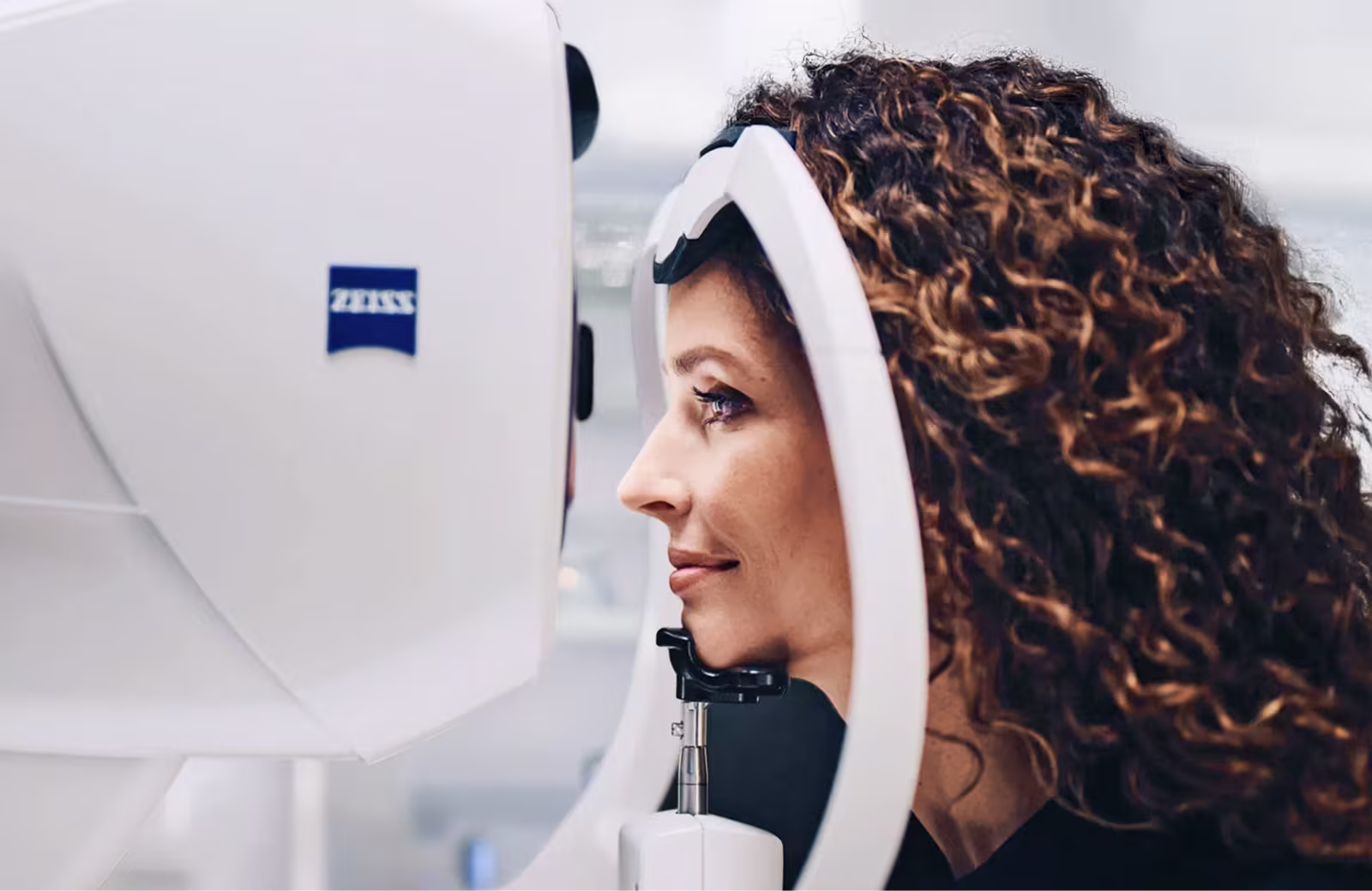 Frau mit lockigem Haar bei einer Augenuntersuchung mit einem Zeiss-Sehtestgerät.
